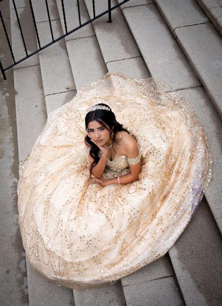 Aerial view of someone wearing an ornate cream-colored ball gown while laying on stone stairs in dramatic poses.