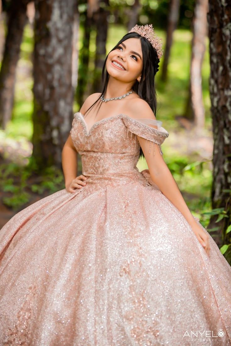 A sparkling rose gold ball gown with off-shoulder detail and glittery sequins photographed in a sunlit forest setting.
