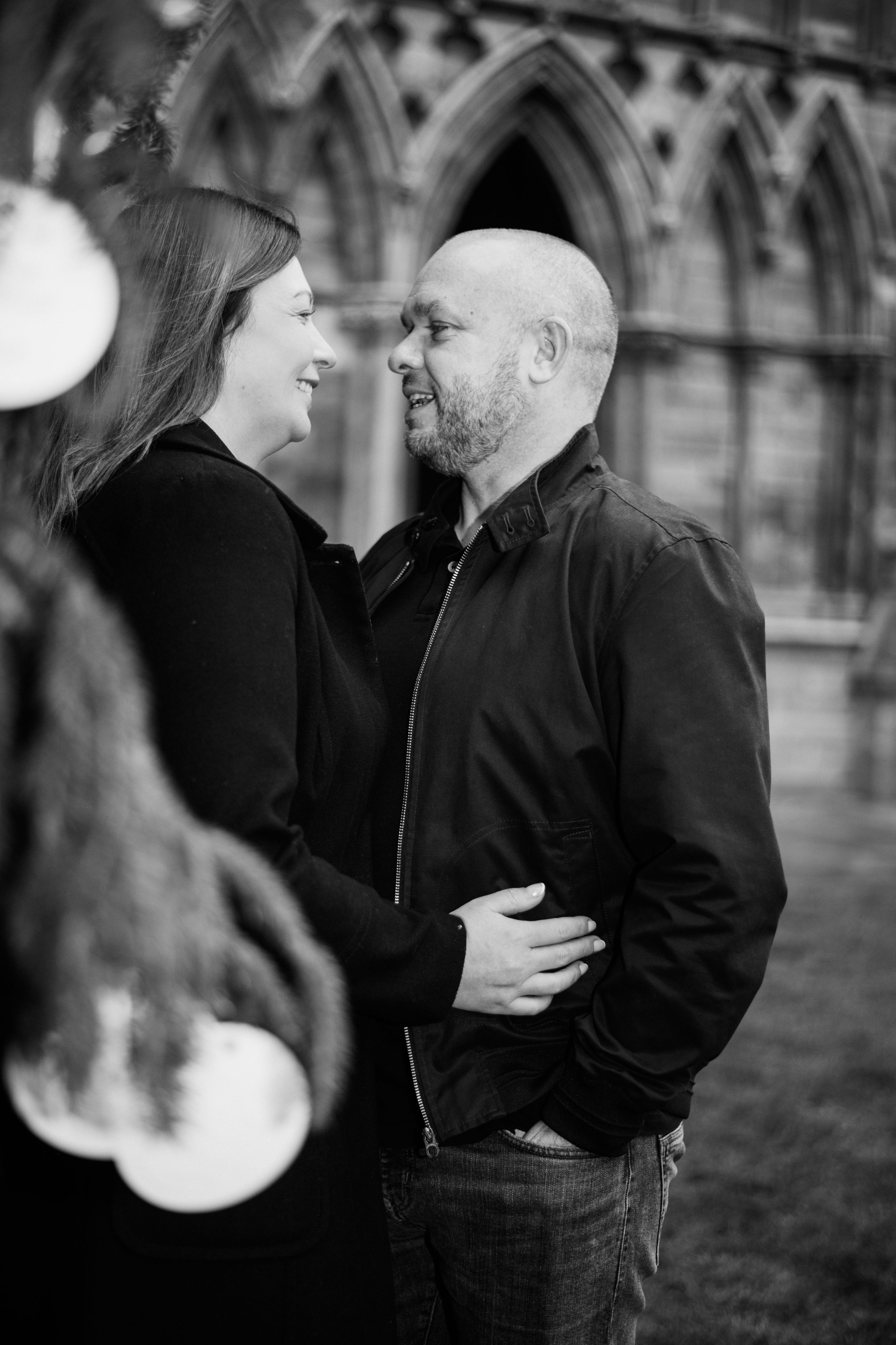 Romantic black and white portrait of a couple sharing a tender moment against gothic architecture.