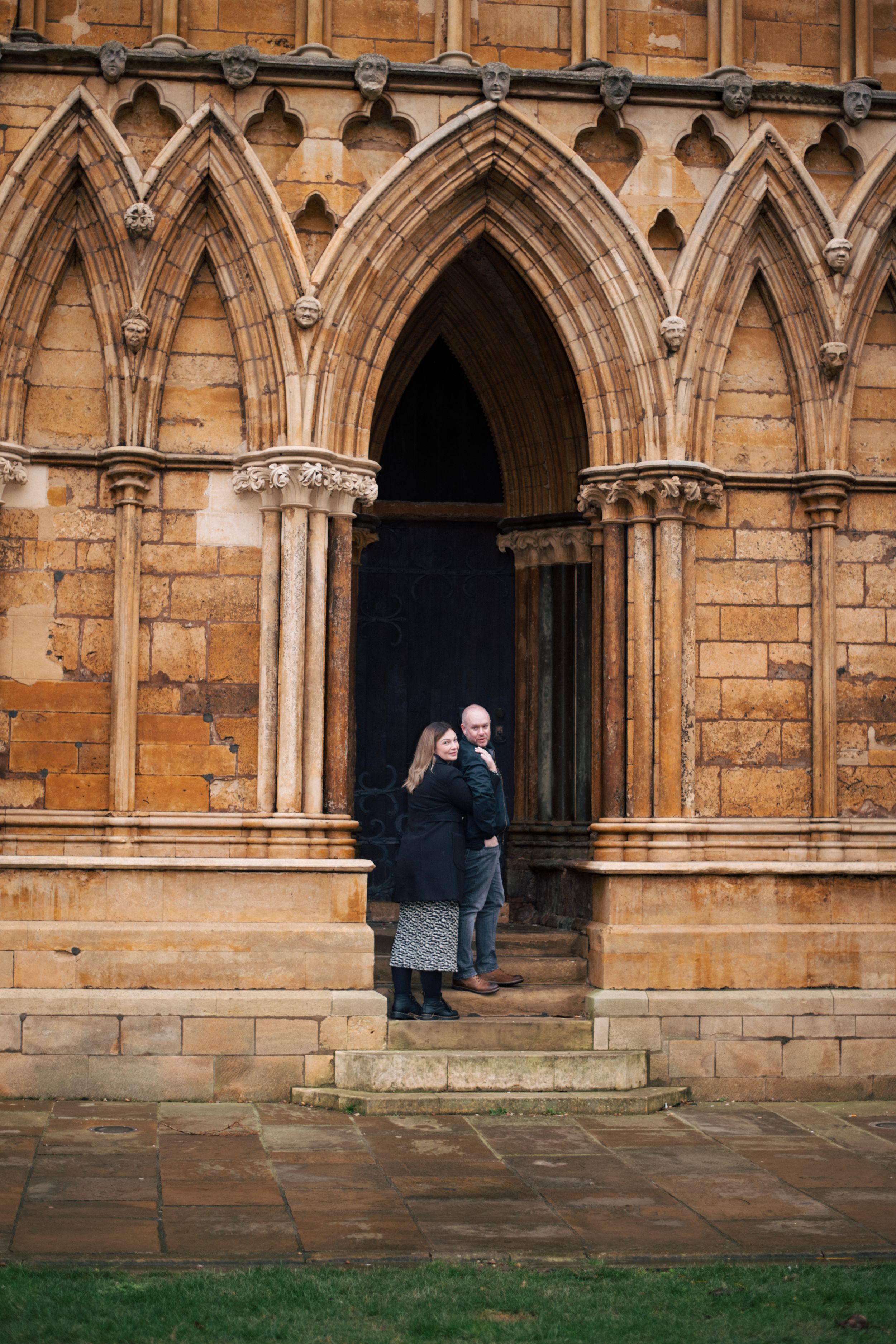 Couple standing in gothic archway entrance of historic stone building.