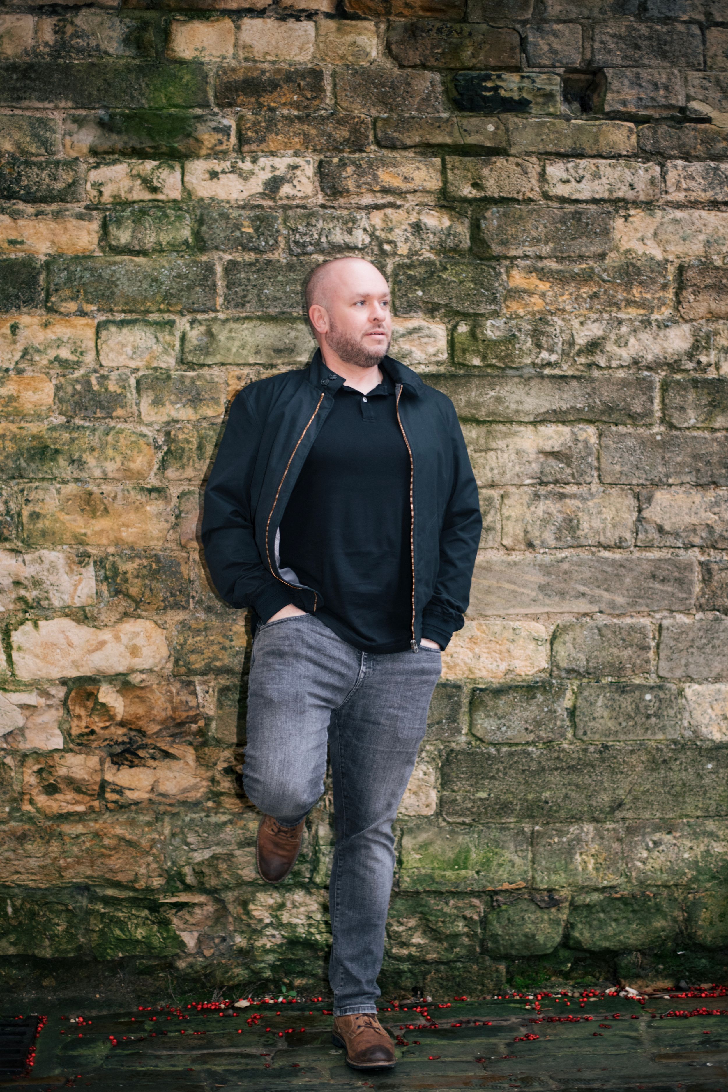 Casual portrait against weathered stone wall with mossy texture.