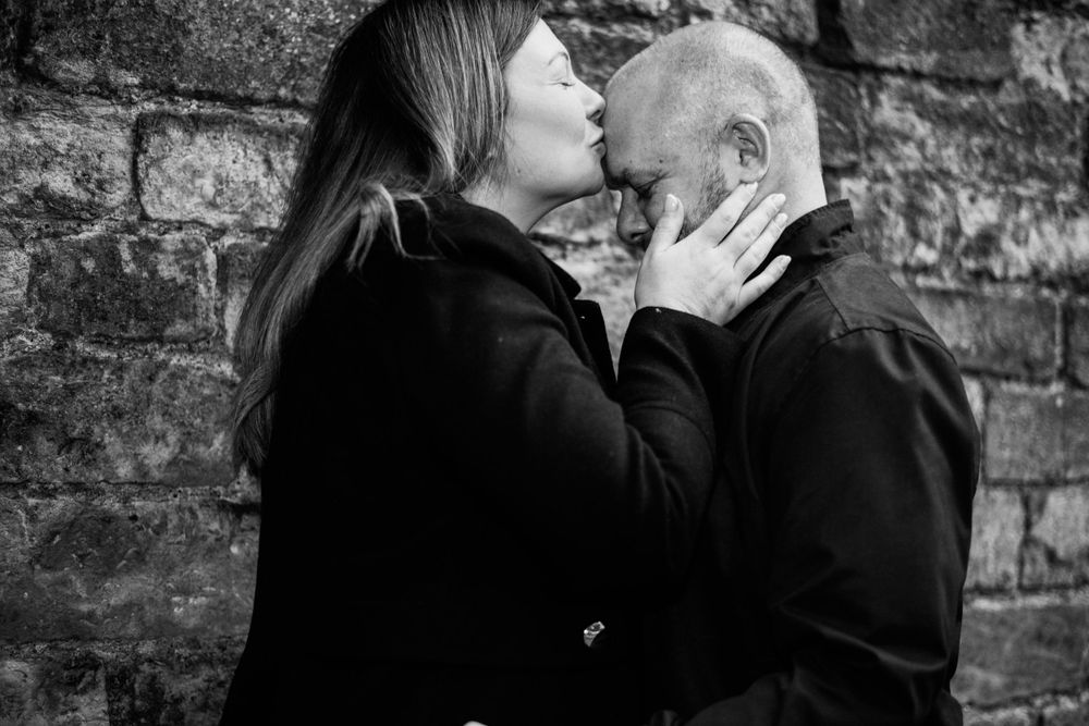 Intimate black and white portrait of couple sharing tender moment against brick wall.