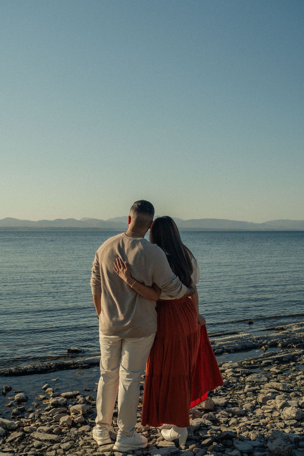 Couple standing together overlooking a serene lake and mountain landscape at sunset.