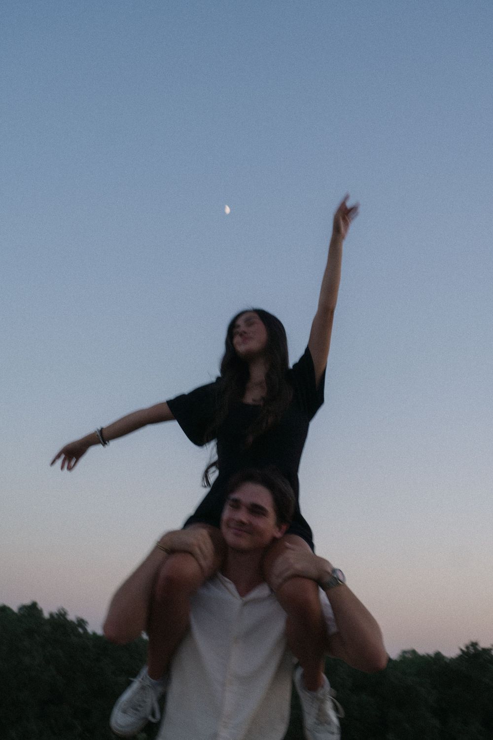 A couple enjoying a playful moment at dusk with one person riding on the other's shoulders.