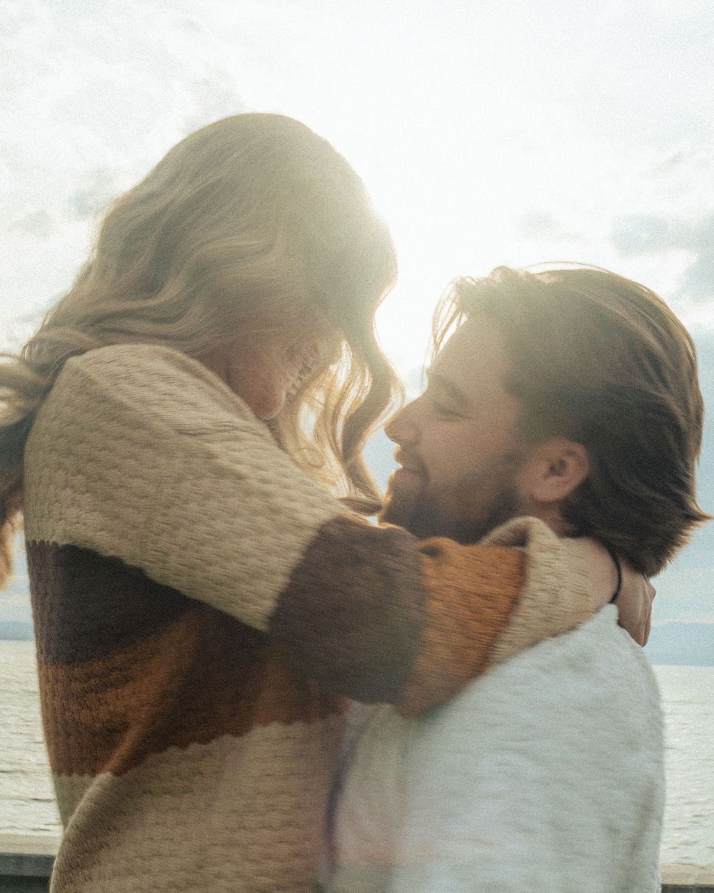 Intimate backlit embrace against ocean backdrop during golden hour.