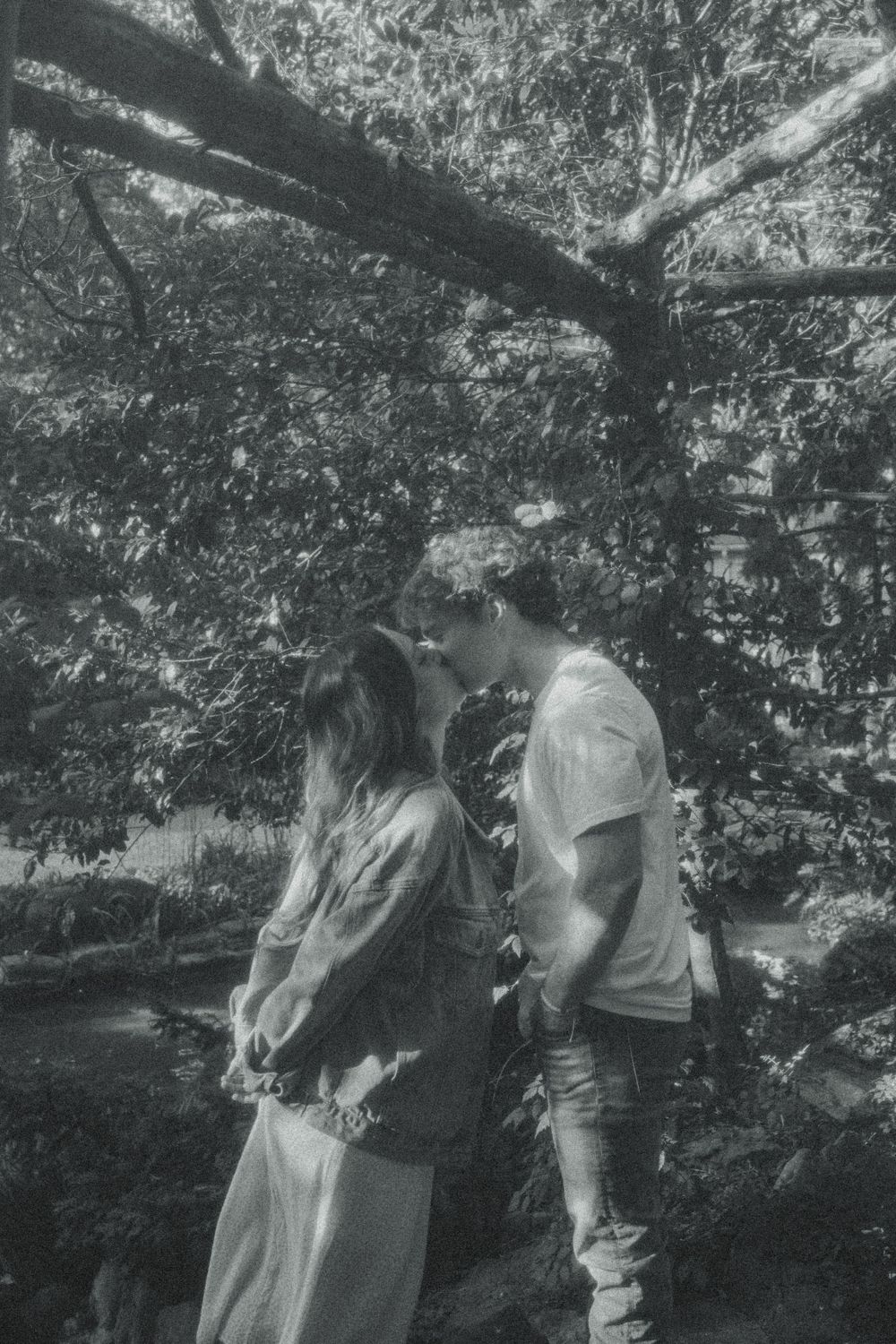 A couple standing close together in a black and white photo under tree branches.