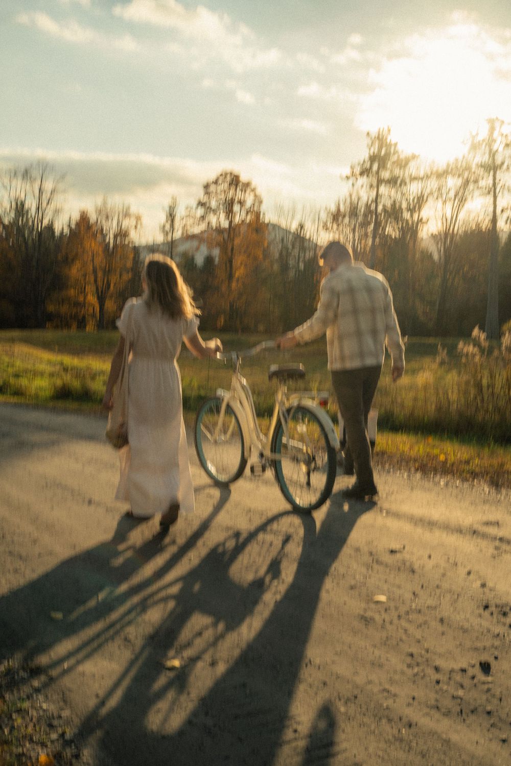 A couple walking with bicycles on a sunlit autumn path casting long shadows.