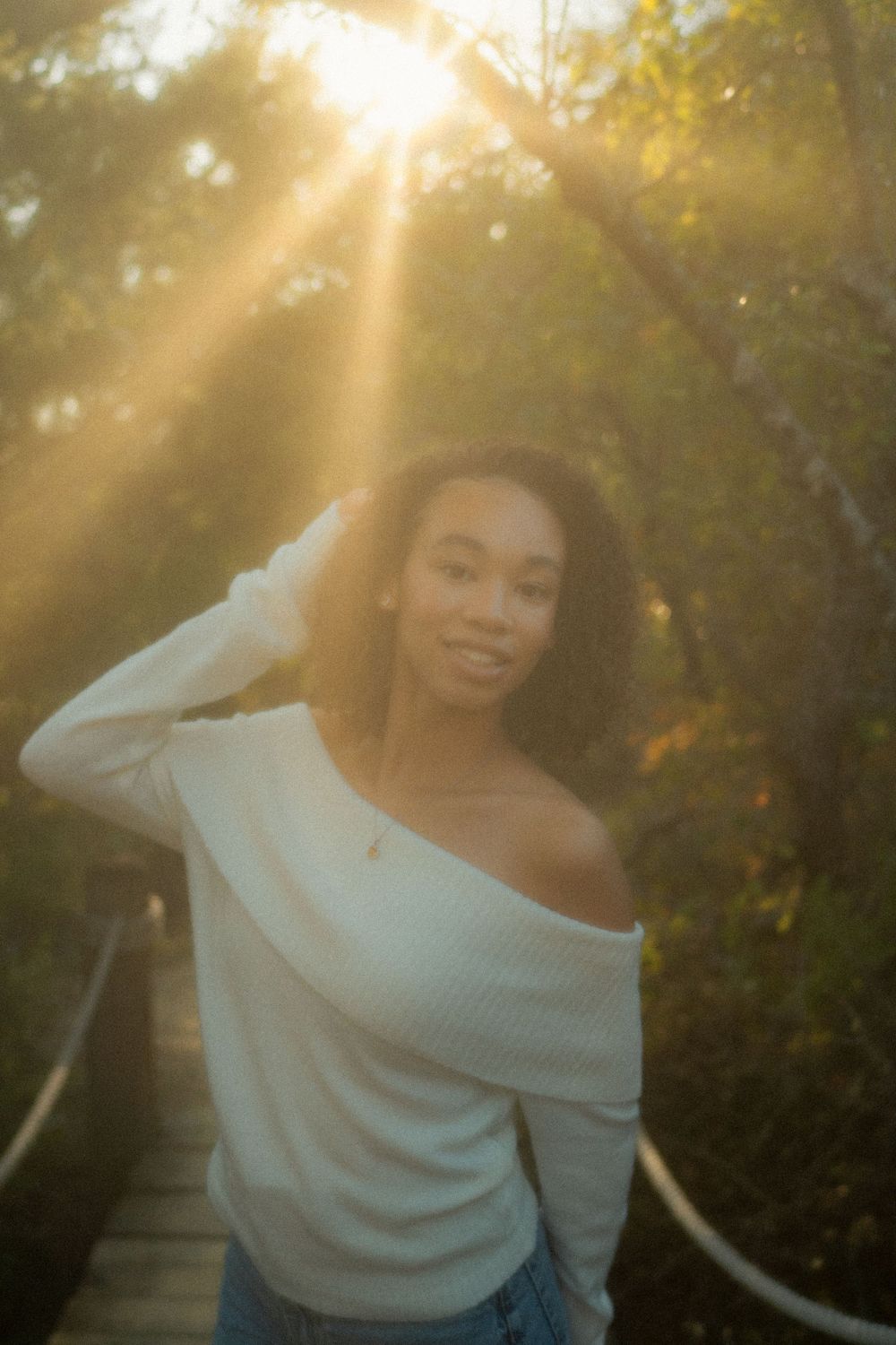 A portrait in golden sunlight on a wooden walkway with sunbeams streaming through trees.