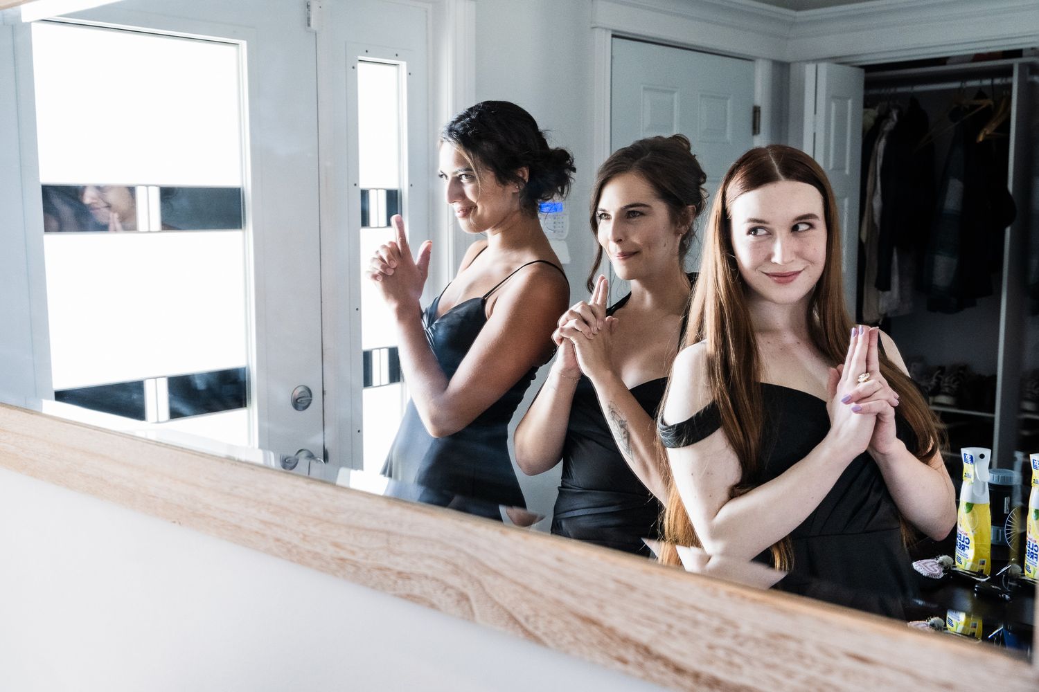 Three bridesmaids striking a Charlie's Angels pose in front of a mirror, their reflections adding a playful touch in St. John's