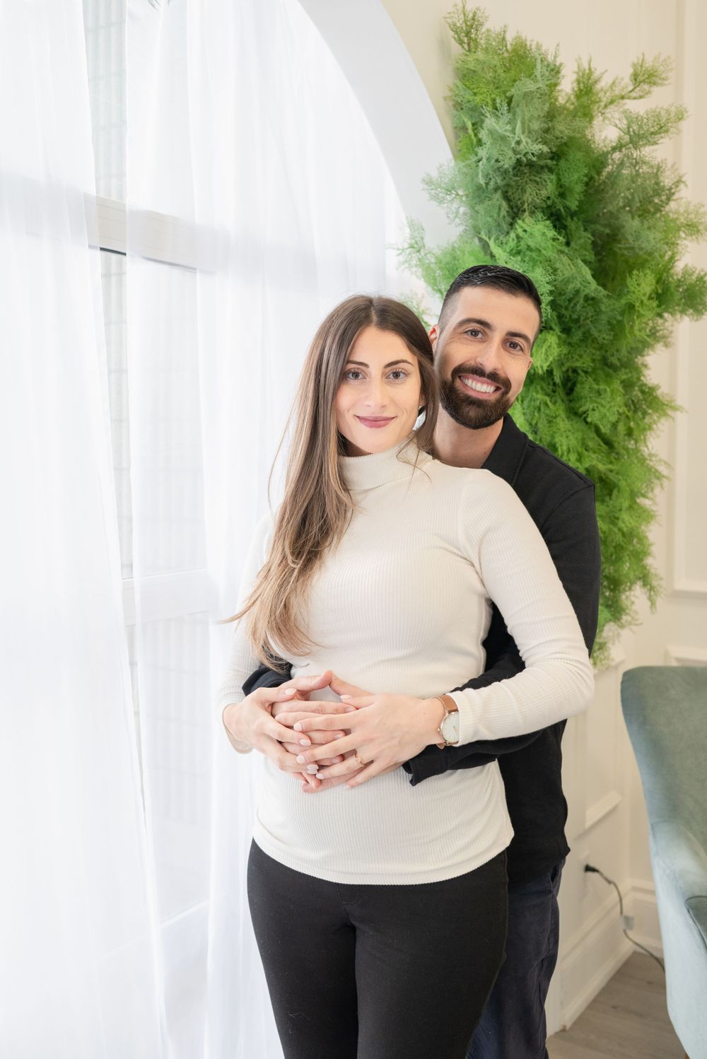 A couple in contrasting black and white outfits poses together near a green plant.