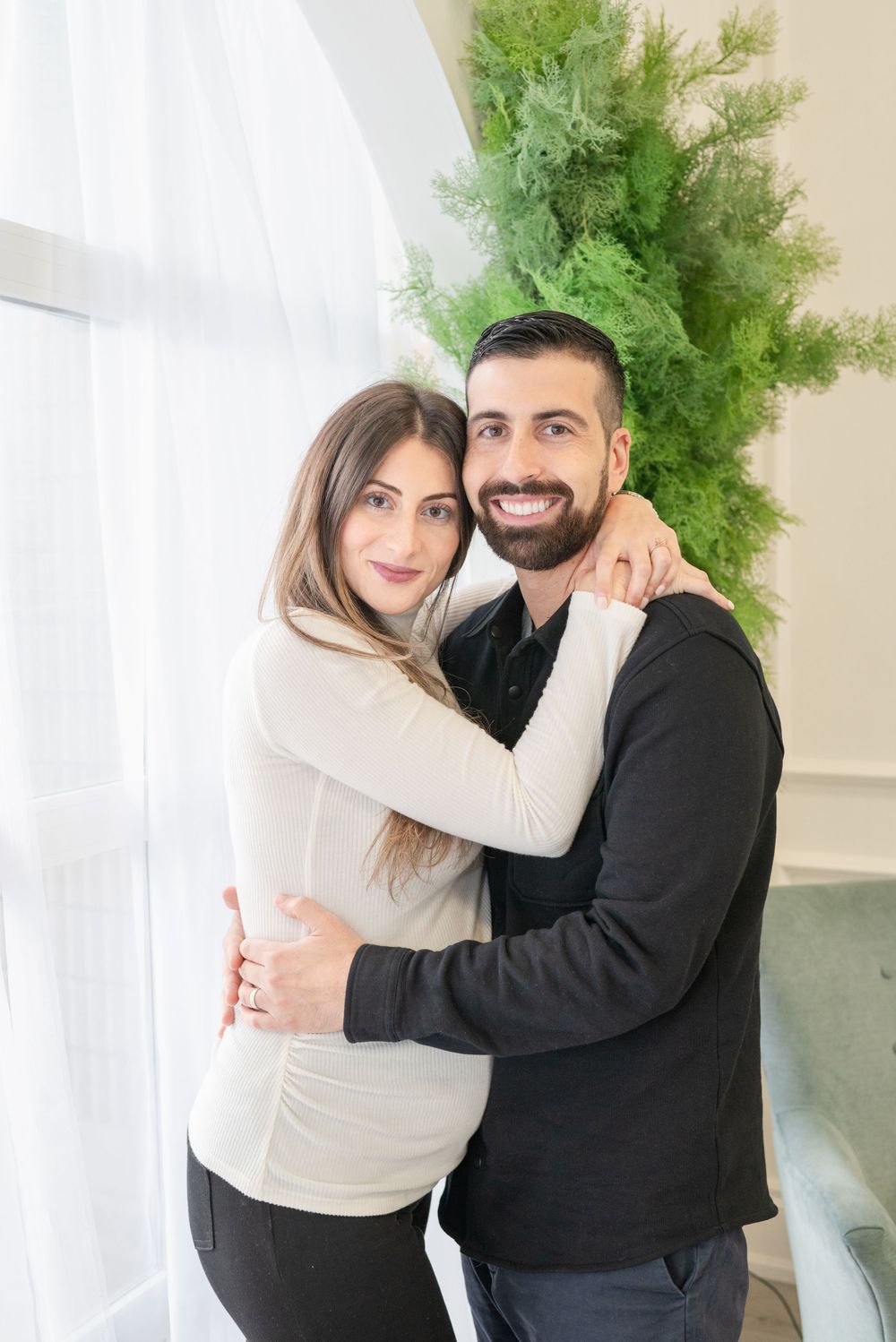 A couple embraces while posing for a portrait next to a tall green plant.