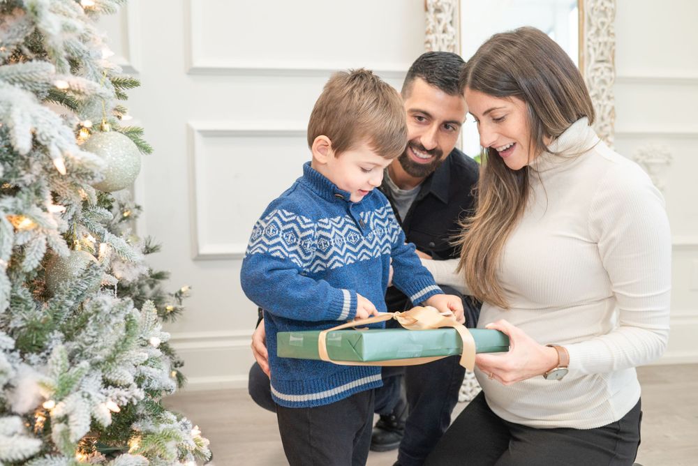 A family opens Christmas presents together near a decorated tree in a bright white room.