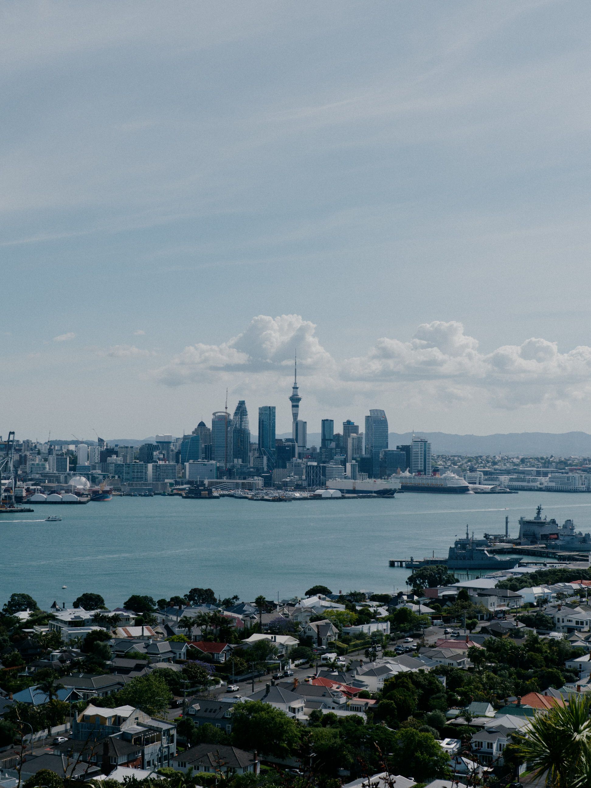 Auckland cityscape with iconic Sky Tower rising above the harbor on a cloudy day.