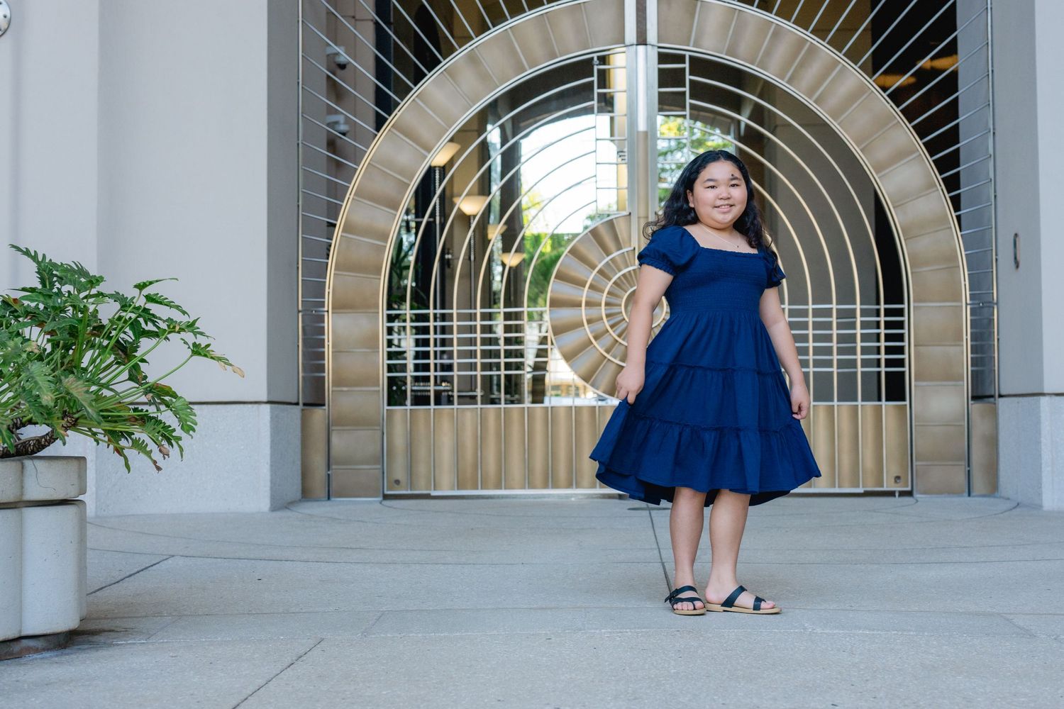 Girl in blue dress in front of gold gate.