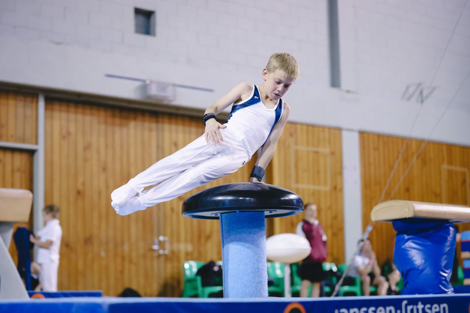 Gymnast performs a split leap over a pommel horse during indoor competition training.