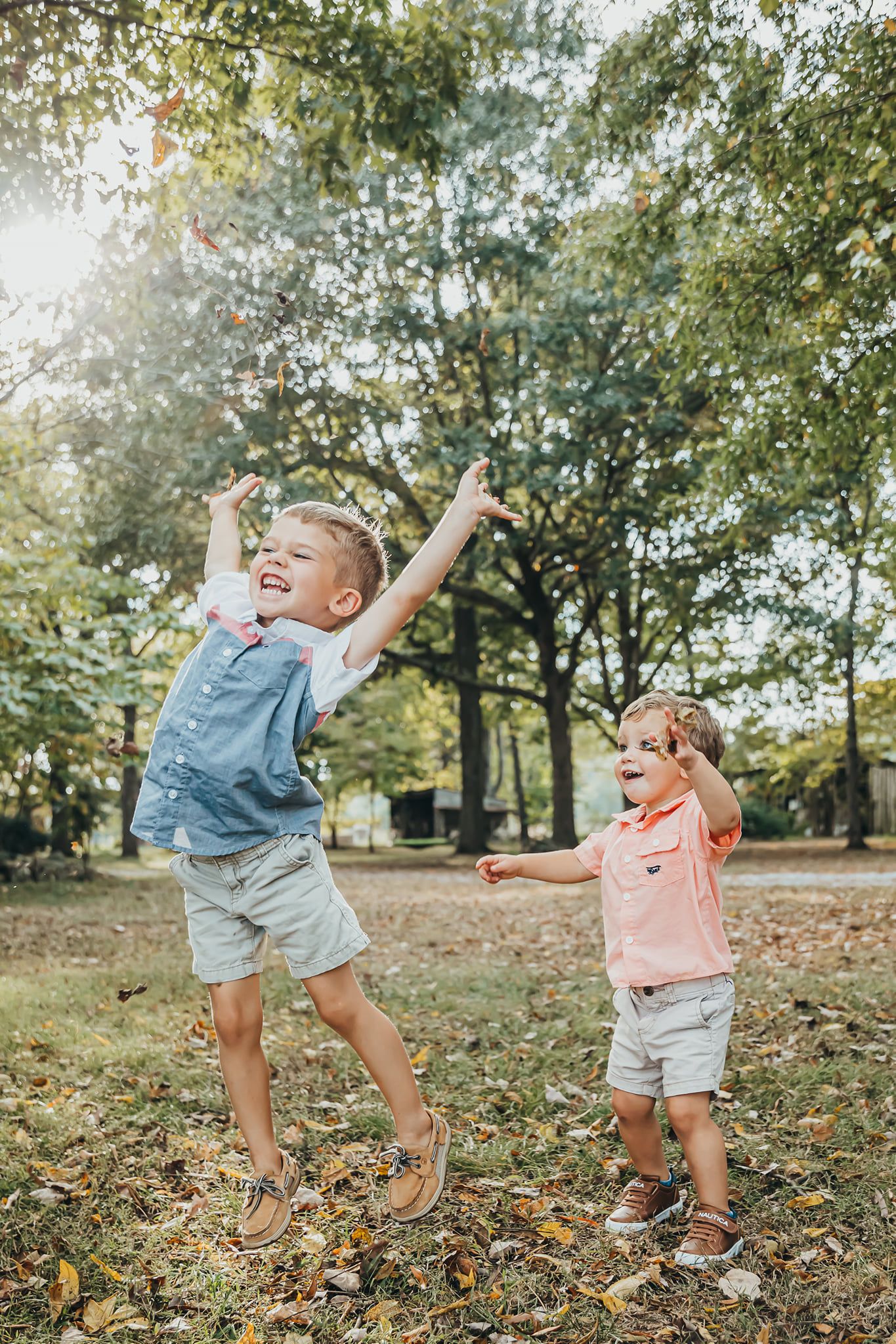 Two children playing and dancing joyfully in autumn leaves at a park.