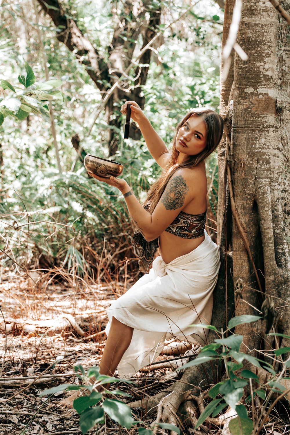 Artistic pose against a tree trunk in a white dress during a tropical forest photoshoot.