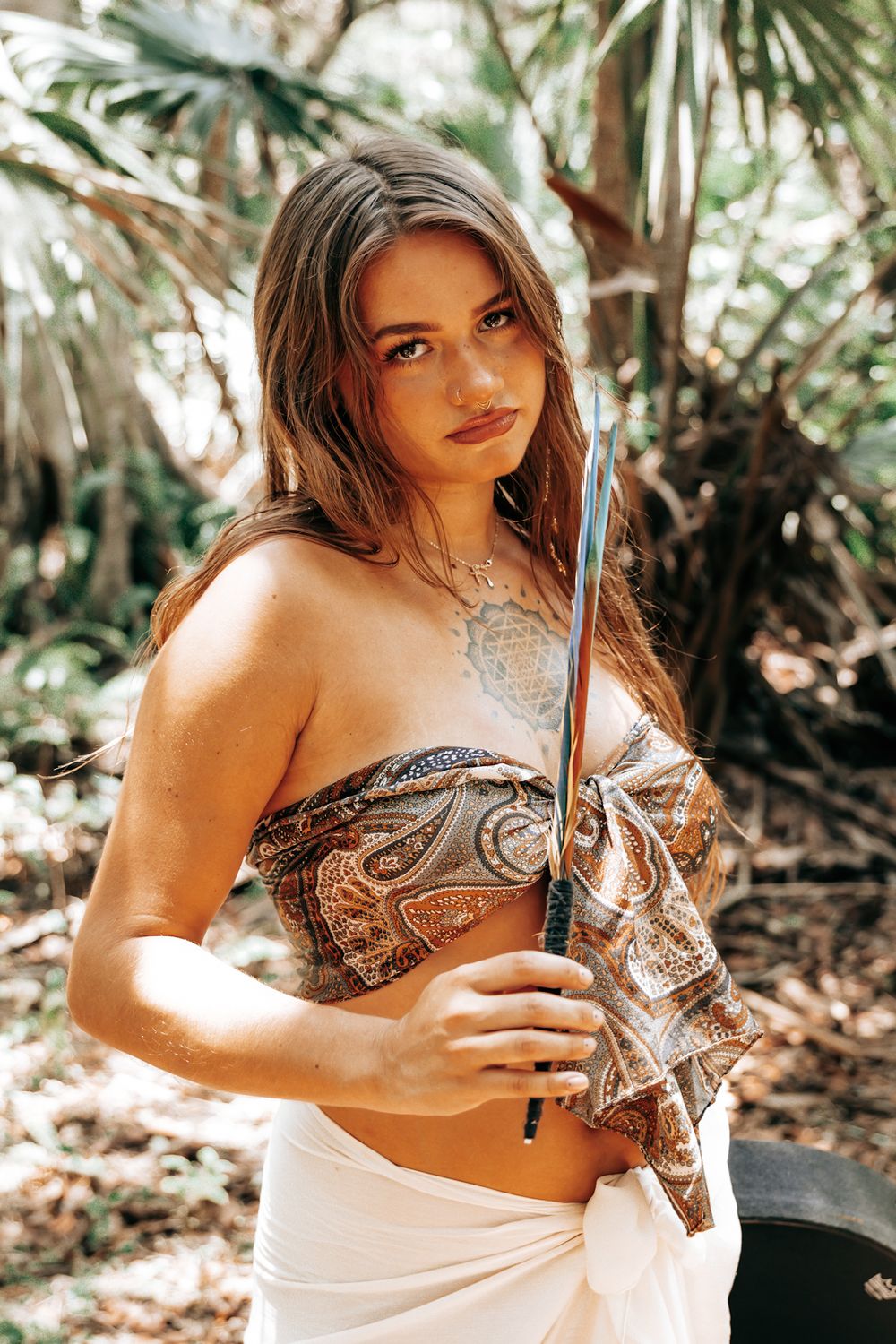 Outdoor fashion photography with ornate clothing and props in a tropical forest setting.