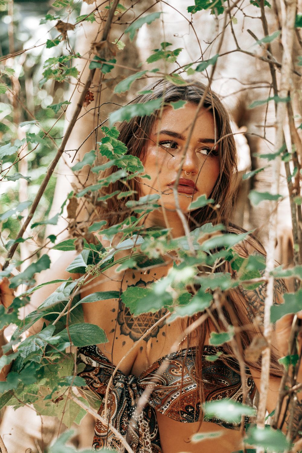 Fashion portrait through green foliage with natural lighting effects.