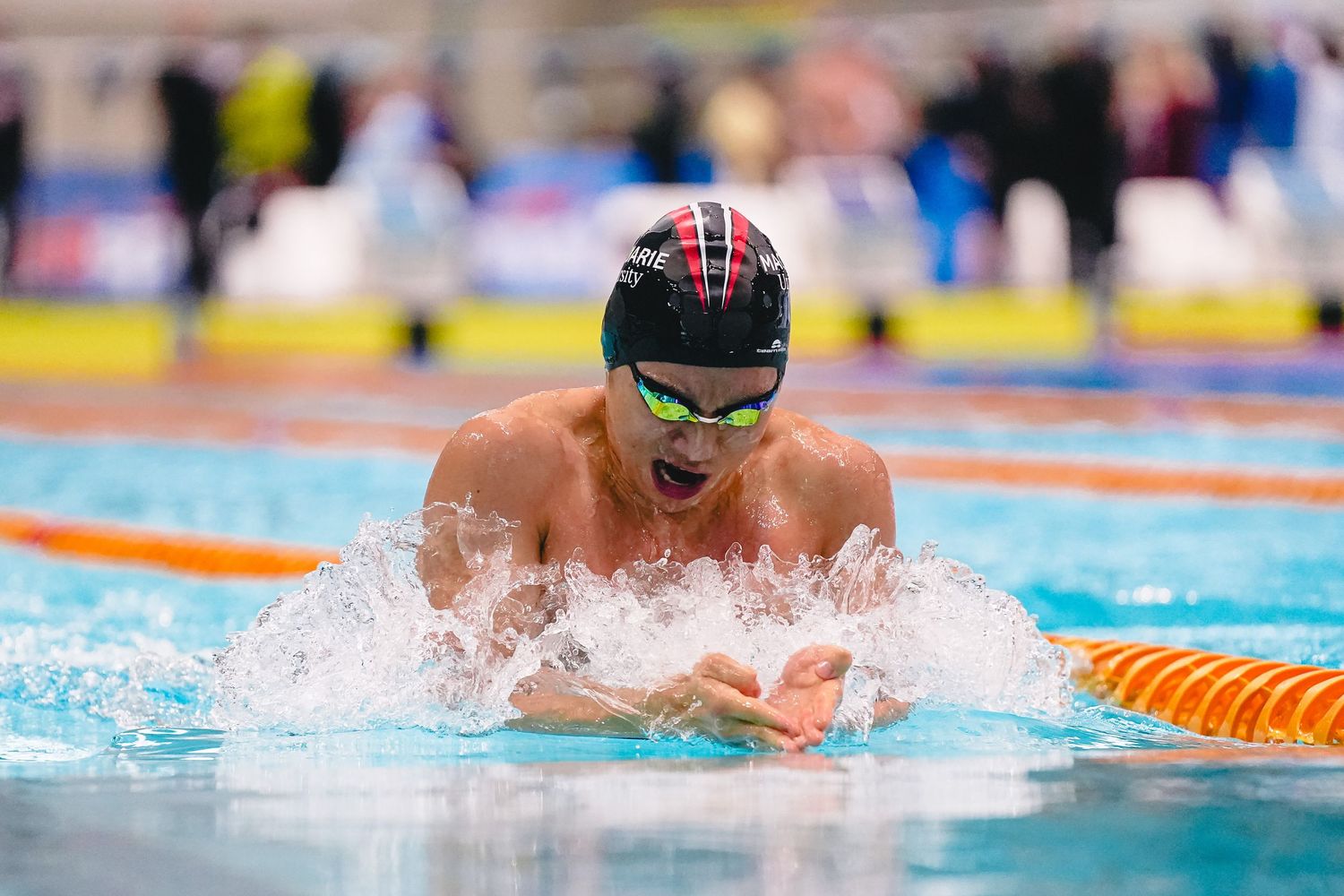 A swimmer sits on a starting block at a competitive swimming event with timing equipment visible.