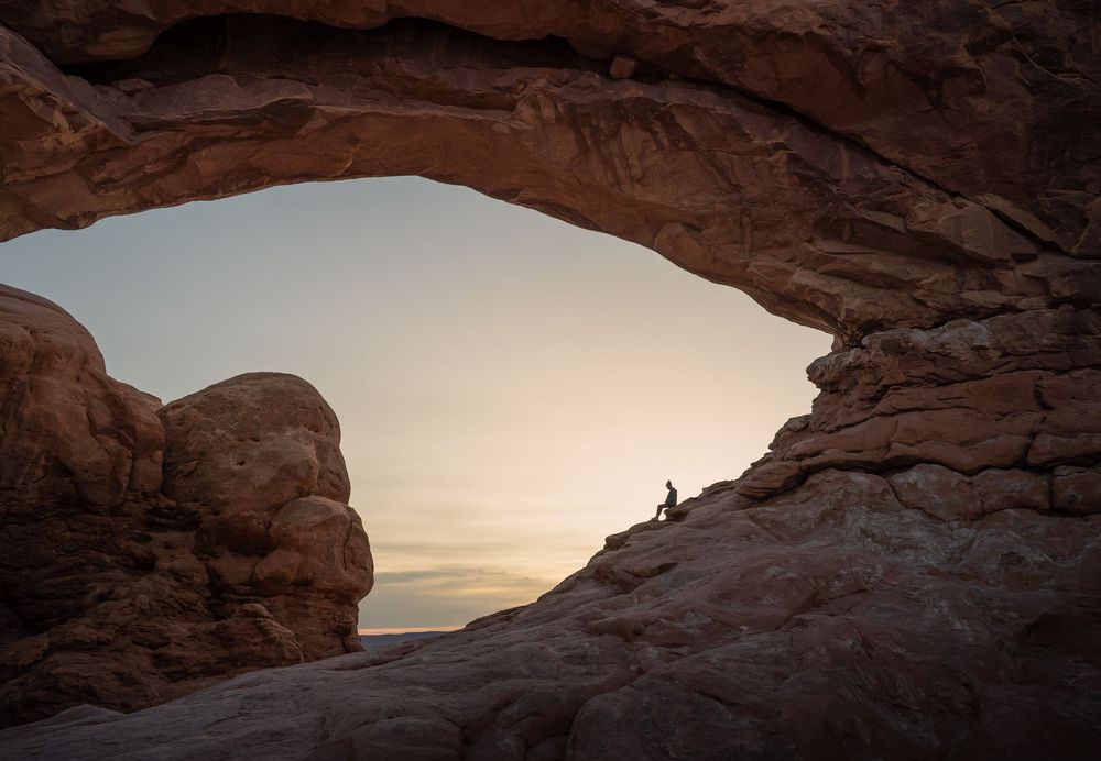 A silhouetted figure stands beneath Mesa Arch in Canyonlands National Park at sunrise, framed by the natural stone formation.