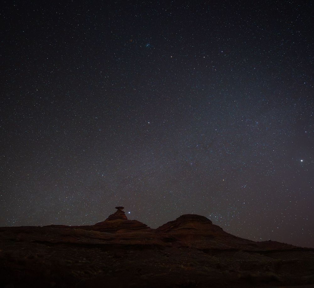 Scenic view of rock formations in the desert at night with a starlit sky stretching across the horizon.