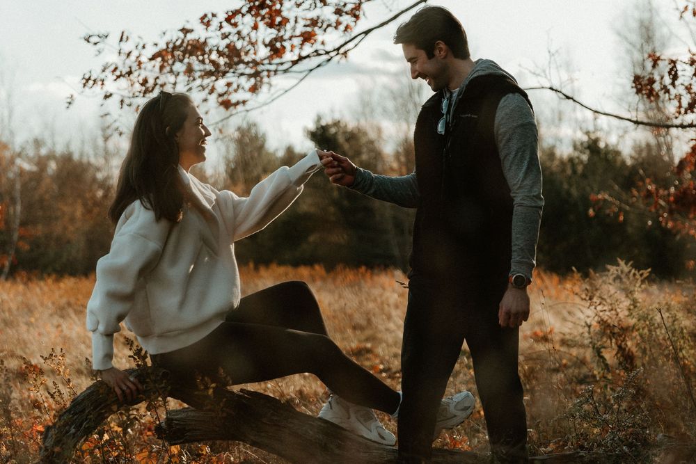 Two people share an intimate moment while sitting on a fallen log in an autumn forest setting.