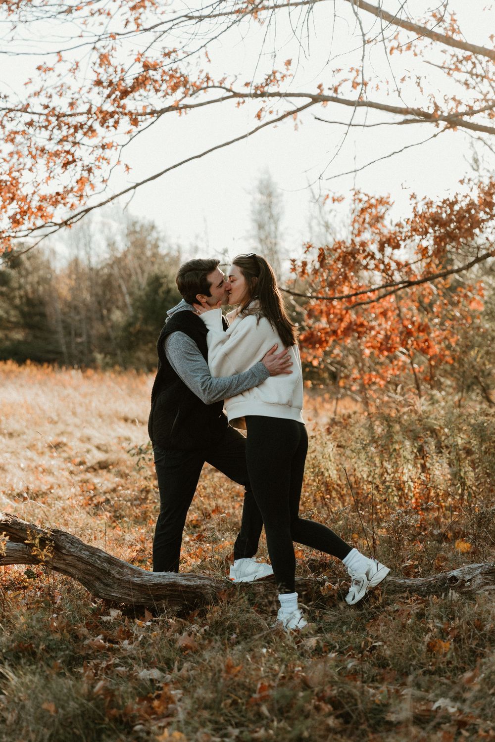 A romantic moment shared on a fallen log surrounded by autumn foliage and golden light.