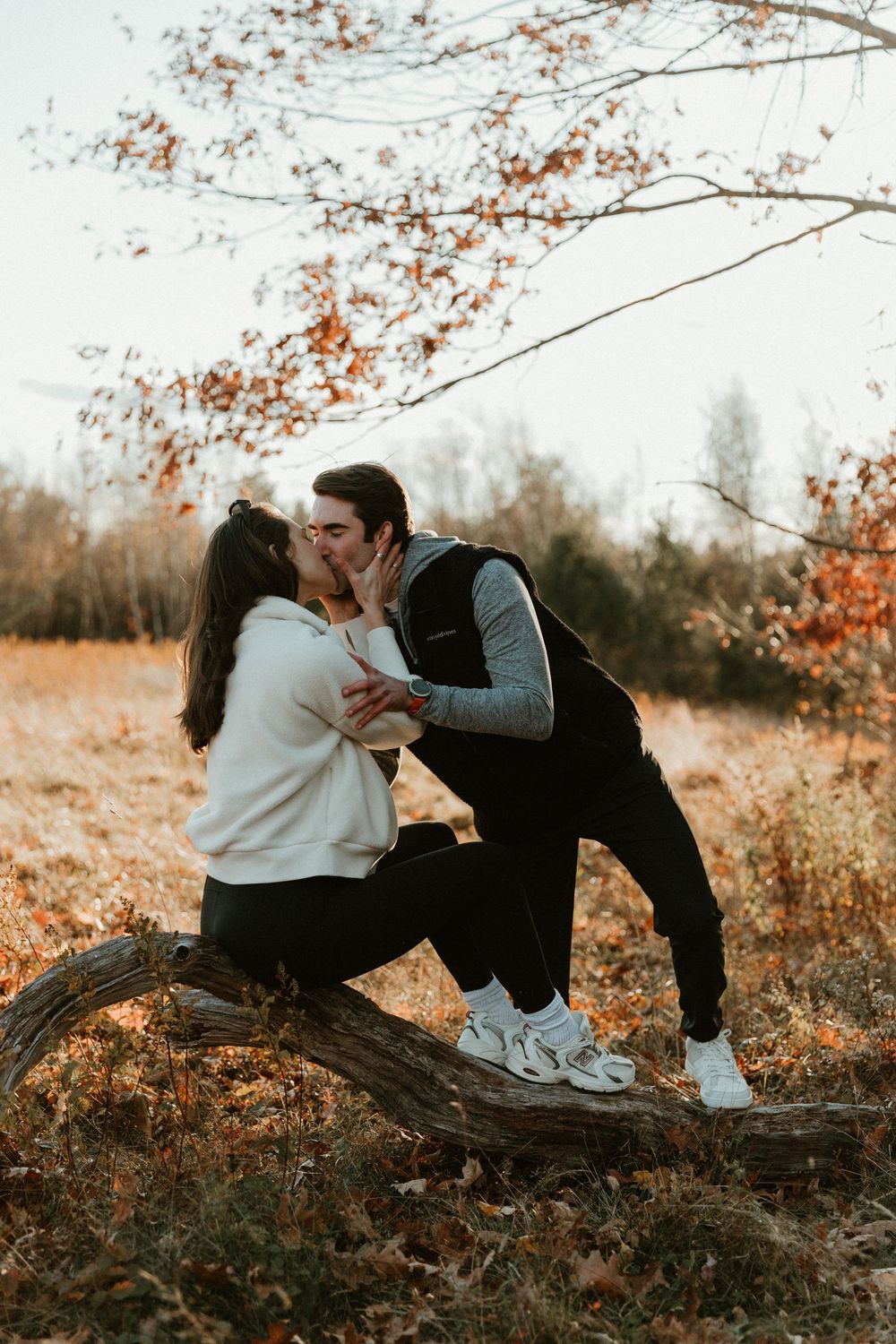 A romantic kiss shared on a fallen tree log during a golden autumn afternoon.