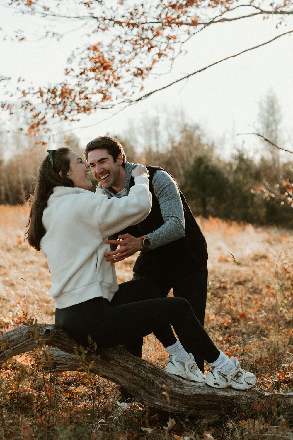 Couple sitting together on fallen log during golden hour in autumn woodland setting.