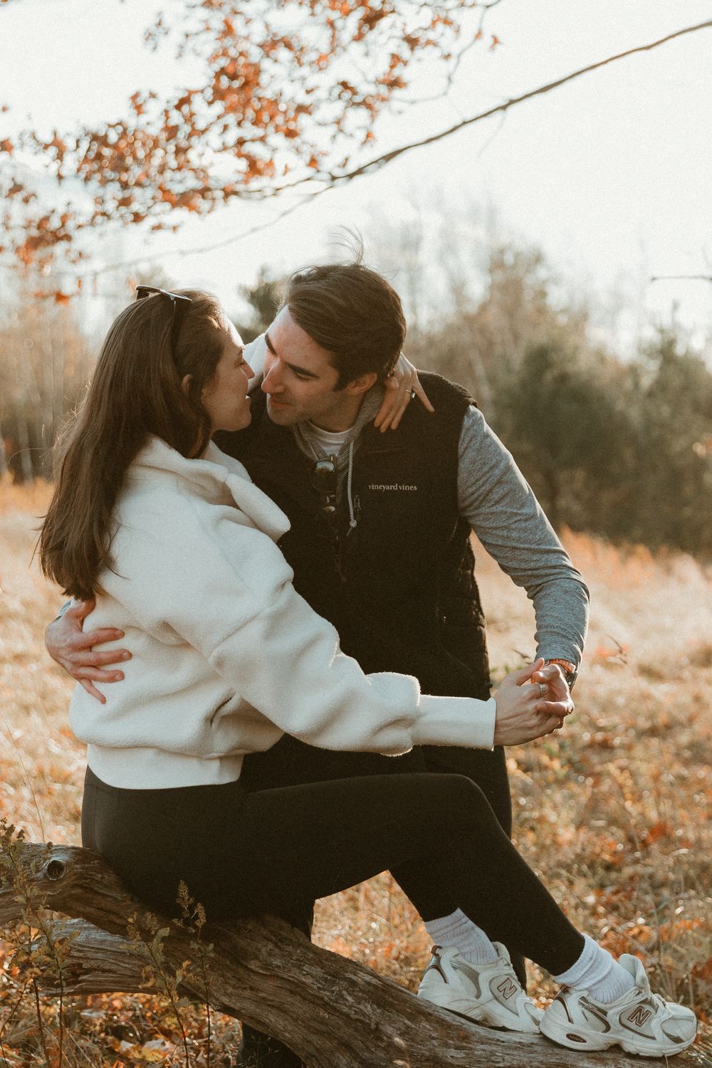 Tender embrace captured in warm autumn light with rustic woodland backdrop.