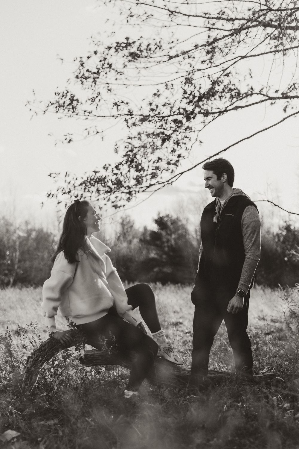 Two people having a conversation in a rustic outdoor setting with bare tree branches overhead.