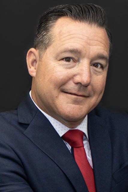 Professional man in navy suit and red tie smiling confidently against dark background.