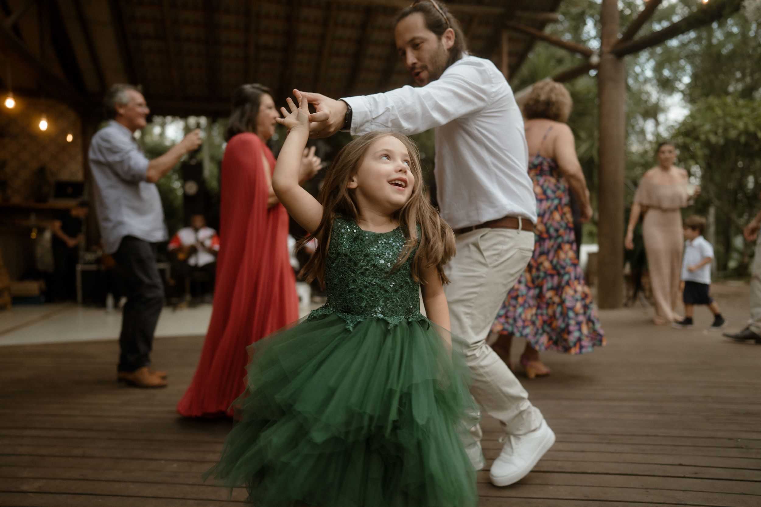 A young dancer in a green tulle dress twirls on a wooden deck during a celebration.