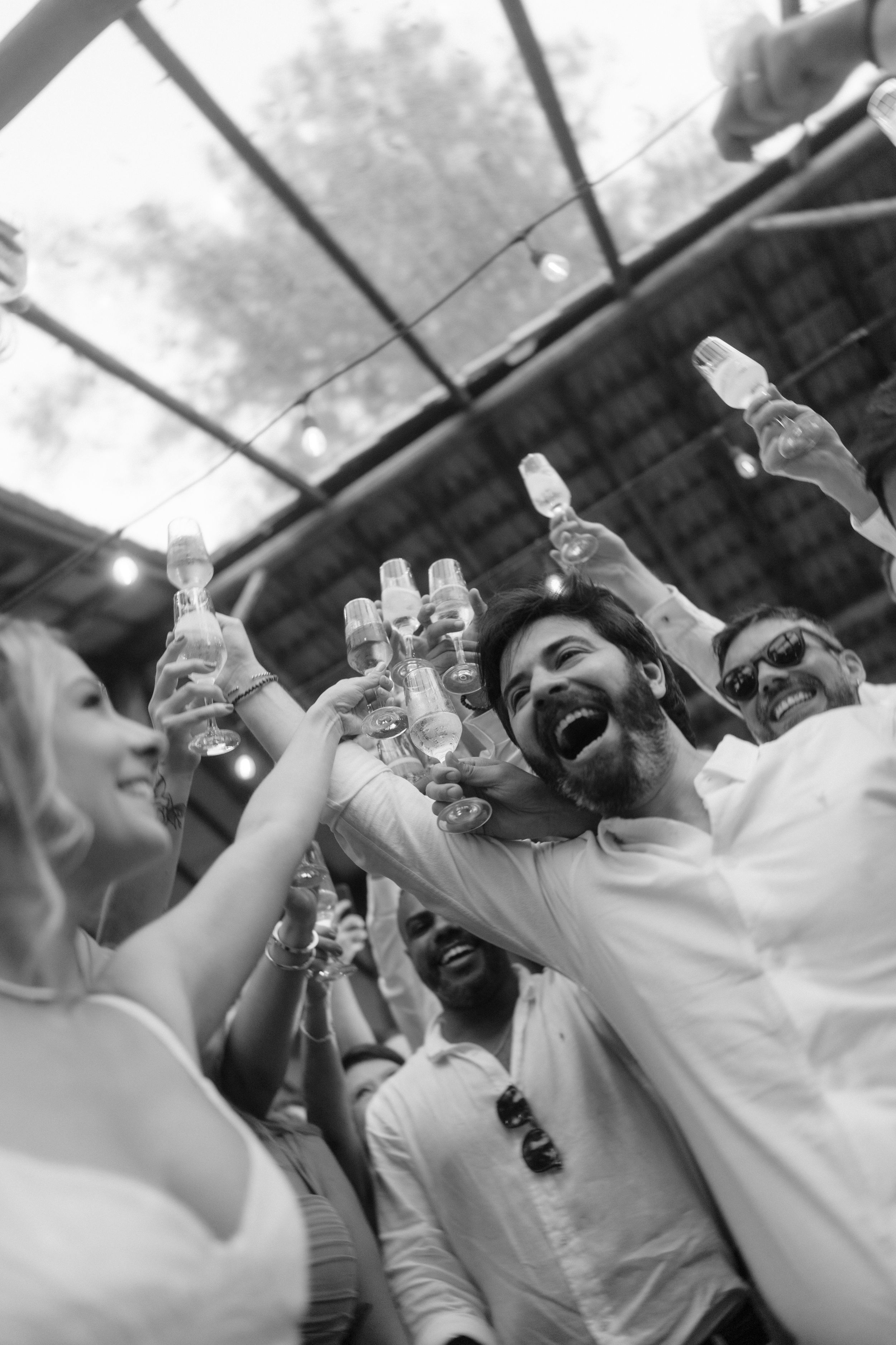 Wedding guests raise champagne glasses in a celebratory toast under a covered venue.