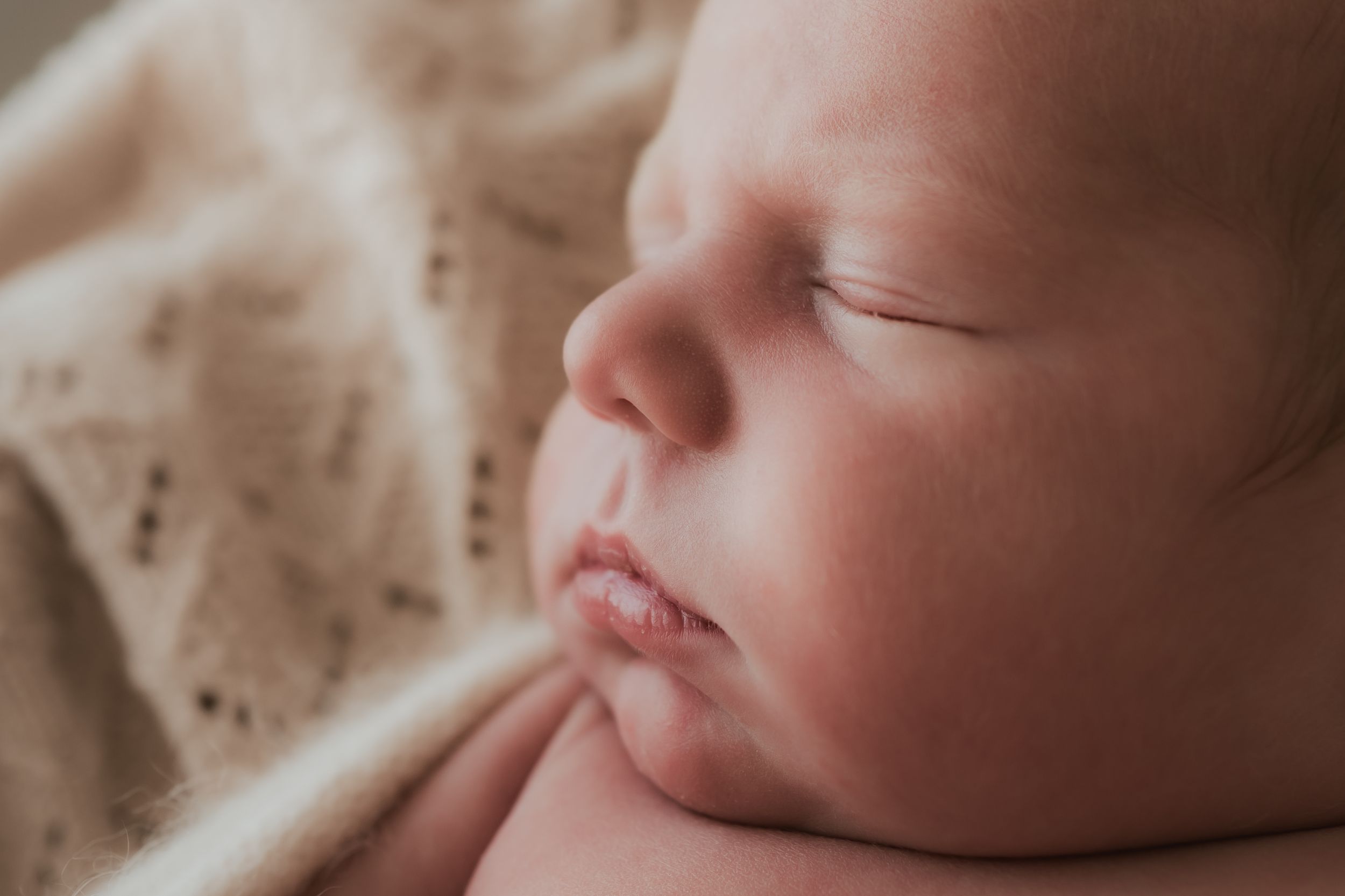 Close-up macro photograph of a sleeping baby's profile face against a beige blanket.