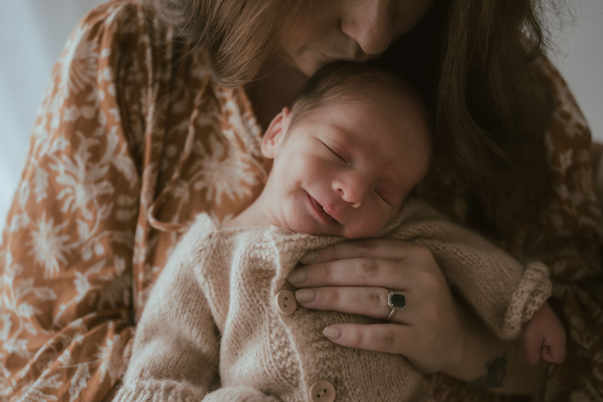 A sleeping newborn baby wrapped in cozy knit clothing rests peacefully in loving arms.
