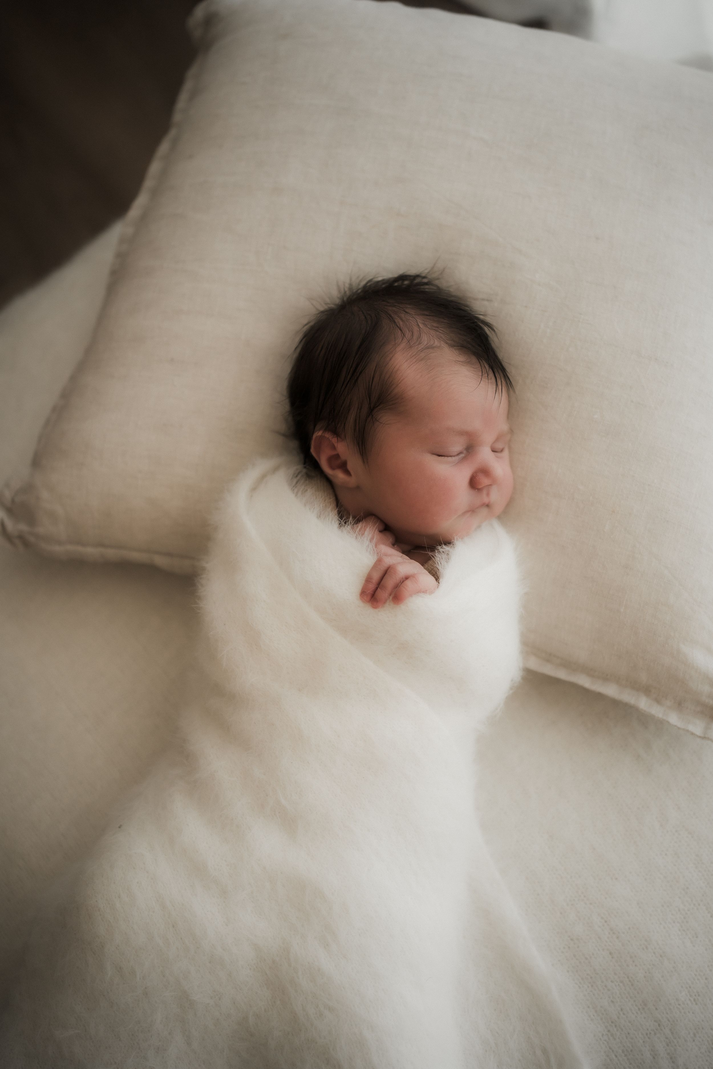 A sleeping newborn peacefully rests on soft white pillows in a minimalist setting.