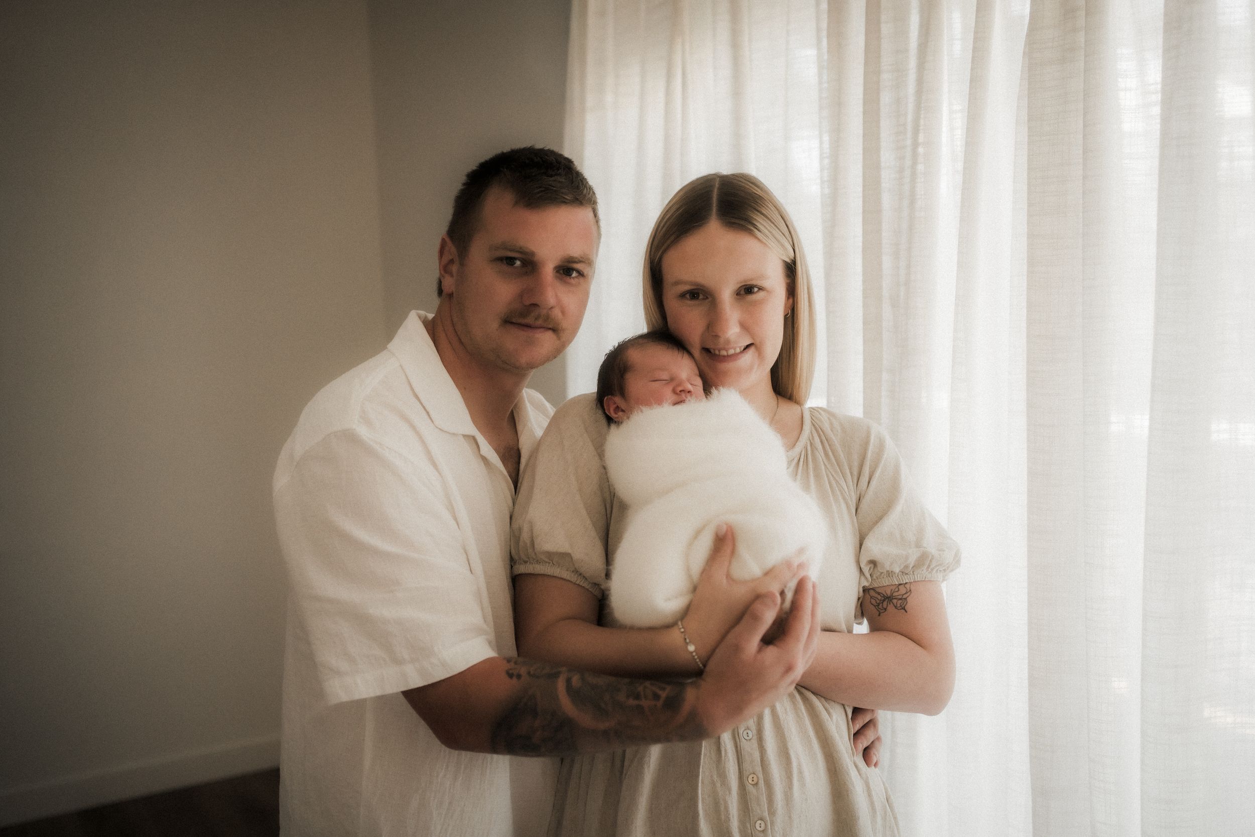 Family wearing white clothing embraces tenderly during an intimate indoor portrait session.