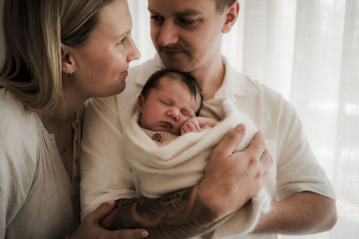 A tender moment of breastfeeding and bonding between parent and children beside a bright window.