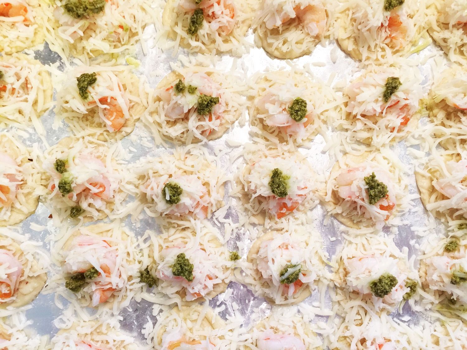 Seafood appetizers topped with pesto and cheese on a light background.
