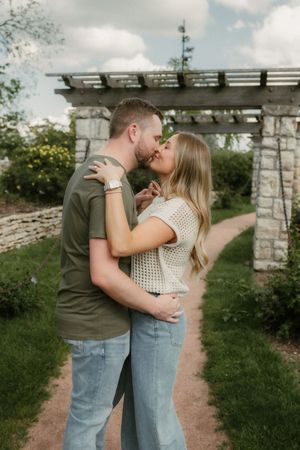 A romantic couple embraces on a garden path beneath a stone pergola on a sunny afternoon at Loose Park Rose Garden in Kansas City.