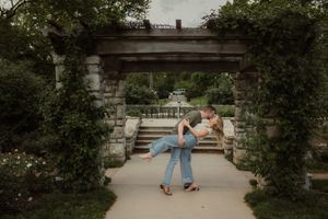 Romantic golden hour portrait of Kansas City couple standing under blooming trees at Loose Park with their pup sitting at their feet.
