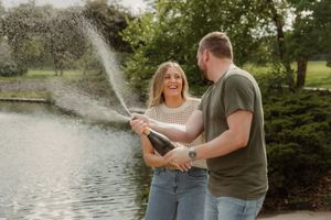 Joyful candid of couple mid-champagne spray, both laughing with arms raised, captured during their Kansas City engagement shoot.