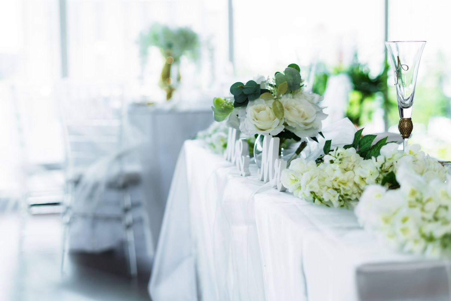 Elegant white floral table arrangements with natural light streaming through windows.