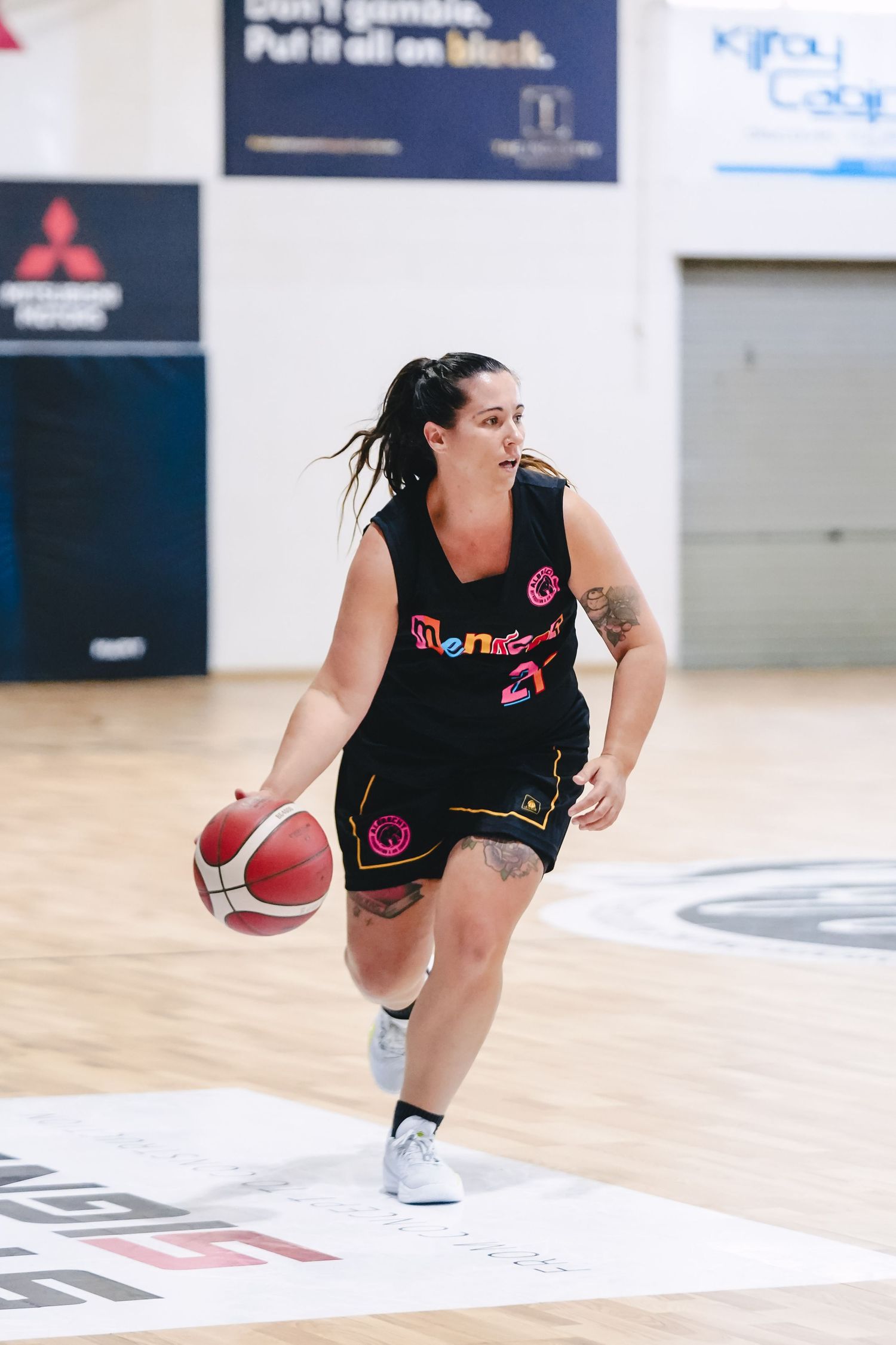 Basketball player dribbles down court wearing black uniform with number 27 during indoor game on wooden floor.
