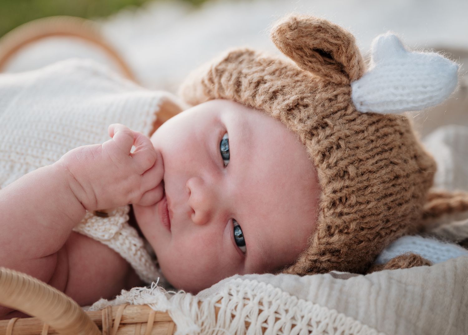 Sweet baby wearing a knitted bear hat with ears lies on white blanket while gazing at camera.