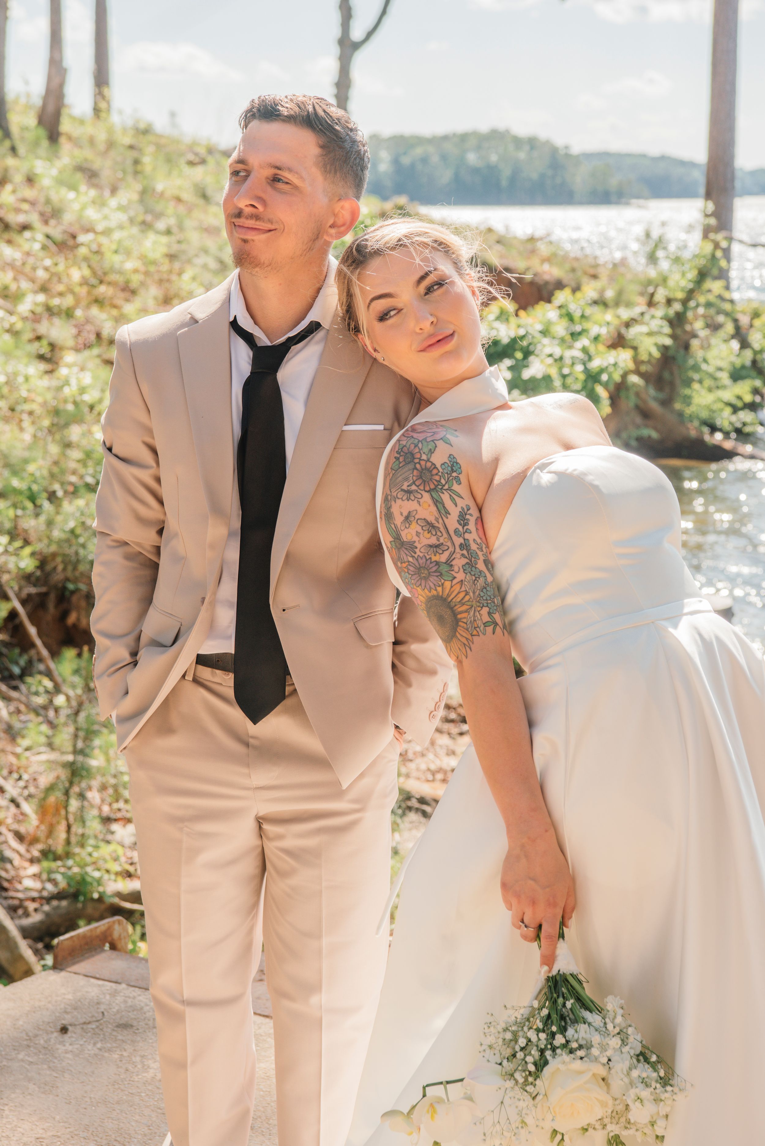 A couple poses together outdoors on their wedding day in formal attire against a scenic natural backdrop.
