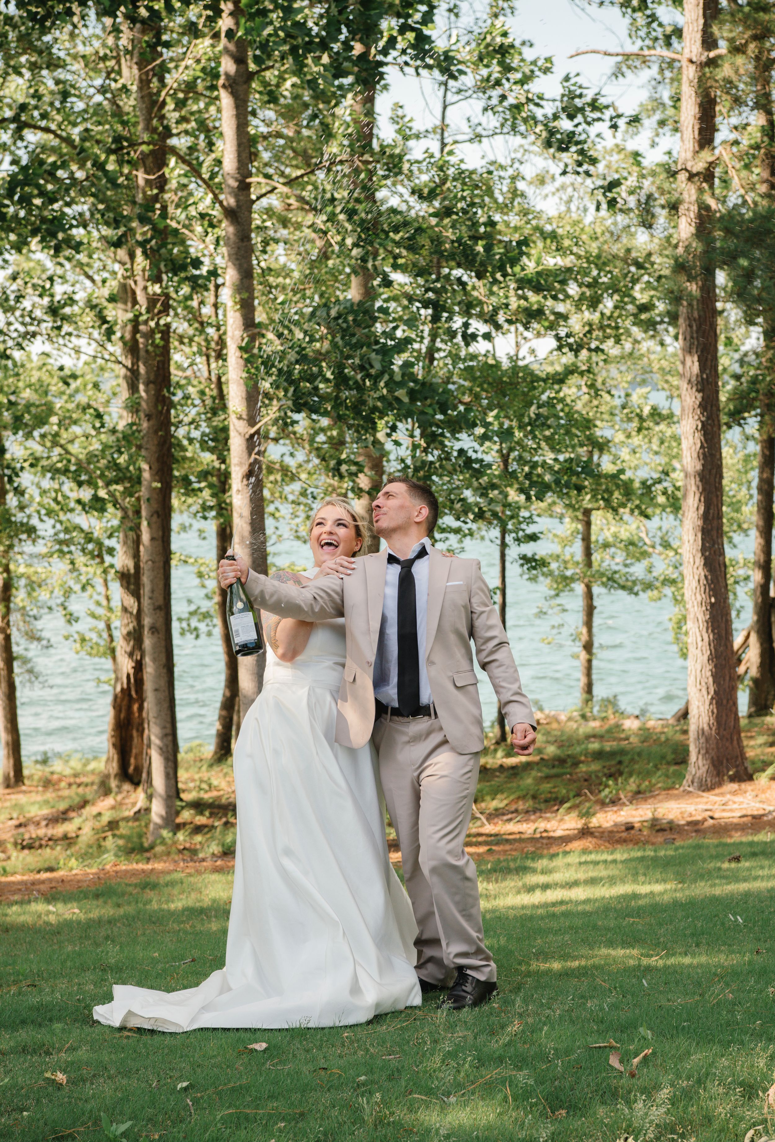 A romantic lakeside wedding with a couple walking together among tall trees and green grass on a sunny day.