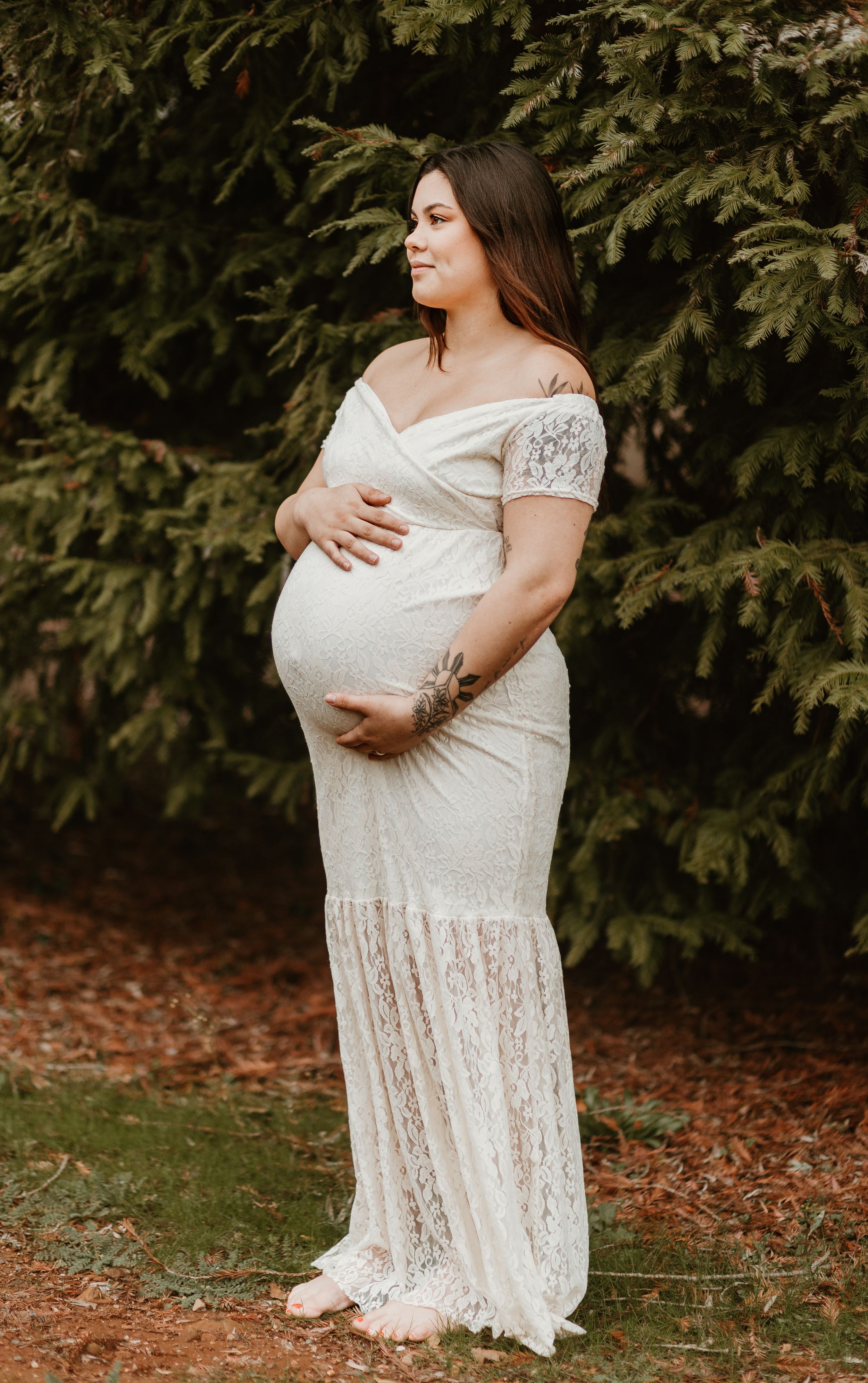 A delicate white lace dress photographed against a backdrop of evergreen trees.